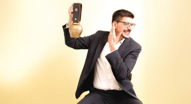 Mann hält Kuhglocke in der Hand und hält sich ein Ohr zu